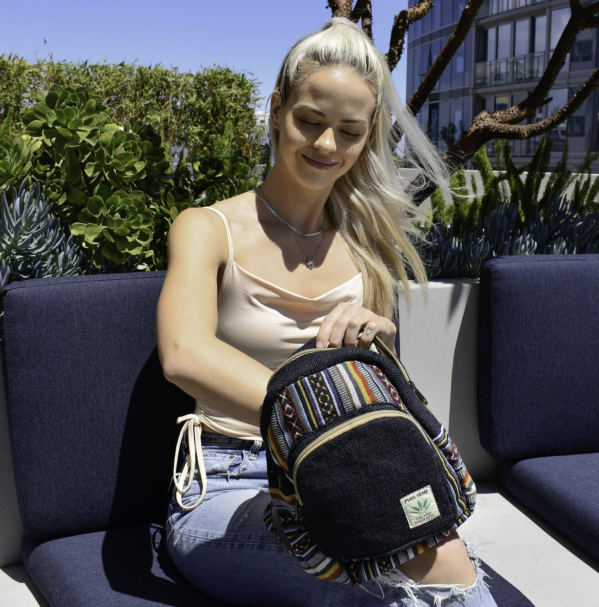 Model holding Freakmandu black hemp mini backpack with colorful Gheri woven trim, outdoor lifestyle photo